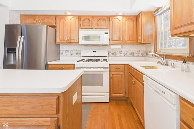 kitchen with light wood-type flooring, a sink, white appliances, and light countertops