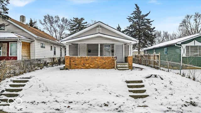 view of front facade featuring covered porch, brick siding, and fence