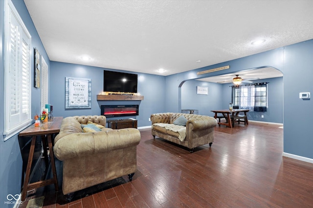 living room featuring ceiling fan, dark wood-type flooring, and a textured ceiling