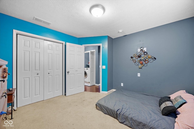 bedroom featuring a closet, a textured ceiling, light colored carpet, and washer / dryer