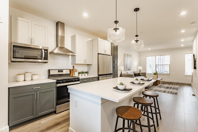 kitchen featuring a breakfast bar, a center island, stainless steel appliances, light countertops, and wall chimney range hood