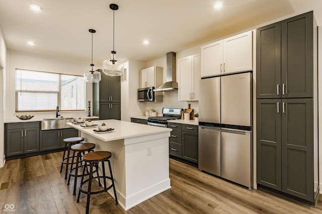 kitchen with a breakfast bar area, a kitchen island, a sink, appliances with stainless steel finishes, and wall chimney exhaust hood