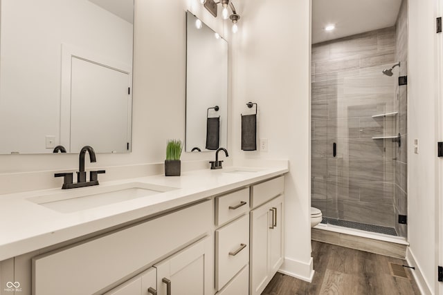 bathroom featuring double vanity, a stall shower, a sink, and wood finished floors