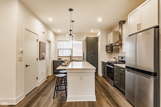 kitchen featuring dark wood finished floors, wall chimney exhaust hood, appliances with stainless steel finishes, a kitchen breakfast bar, and light countertops