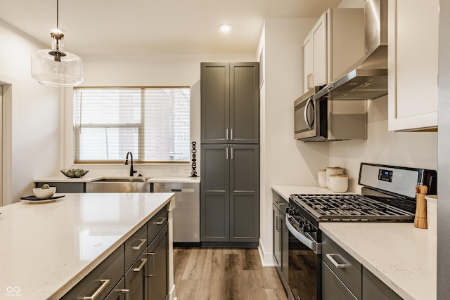 kitchen featuring light stone counters, stainless steel appliances, light wood-style flooring, a sink, and wall chimney exhaust hood