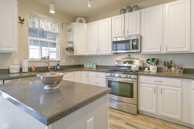 kitchen featuring white cabinetry, a sink, appliances with stainless steel finishes, dark countertops, and light wood-style floors