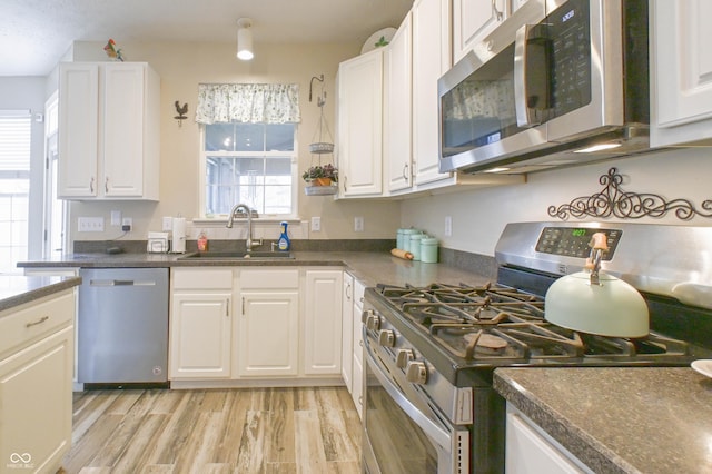 kitchen featuring a sink, light wood-type flooring, white cabinetry, dark countertops, and appliances with stainless steel finishes