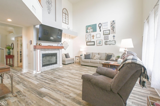 living area with baseboards, recessed lighting, a towering ceiling, wood finished floors, and a tiled fireplace
