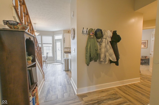 hallway featuring a textured ceiling, wood finished floors, and baseboards