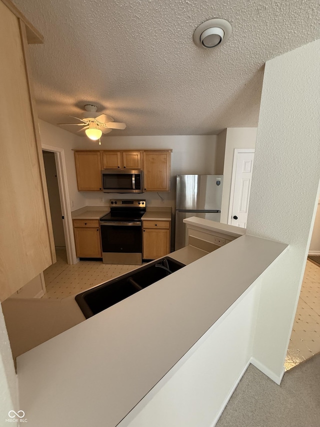 kitchen with appliances with stainless steel finishes, a textured ceiling, ceiling fan, sink, and light colored carpet