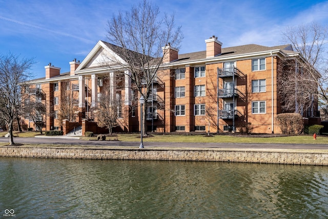 exterior space featuring a water view, a chimney, and brick siding