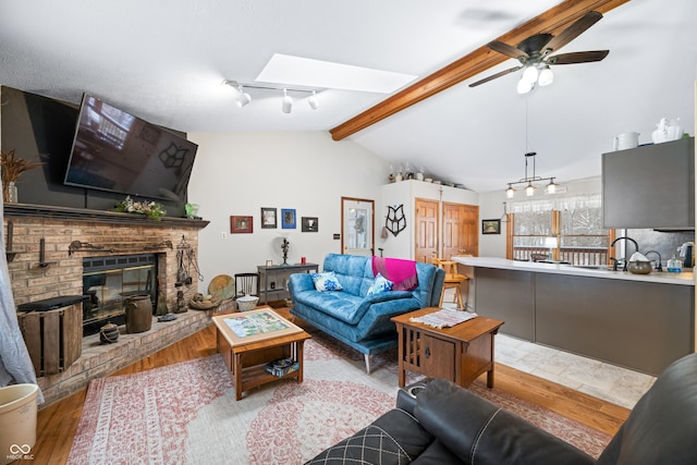 living area featuring a ceiling fan, light wood-type flooring, a brick fireplace, lofted ceiling with skylight, and track lighting