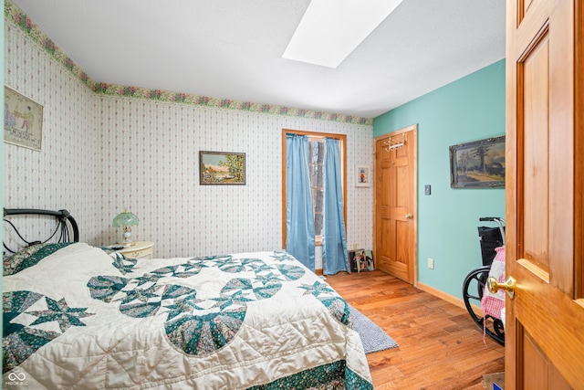 bedroom with wallpapered walls, light wood-style flooring, a skylight, and baseboards