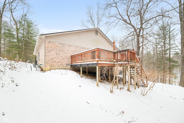 snow covered rear of property featuring stairway, brick siding, and a deck