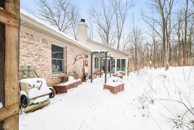 snow covered house featuring brick siding, a chimney, and a pergola