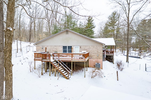 snow covered house featuring cooling unit, brick siding, a deck, and stairs