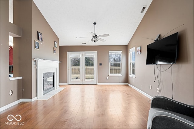 unfurnished living room with vaulted ceiling, ceiling fan, wood finished floors, a tile fireplace, and baseboards