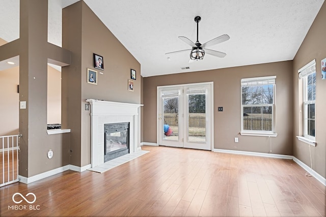 unfurnished living room with baseboards, a tile fireplace, lofted ceiling, wood finished floors, and a textured ceiling