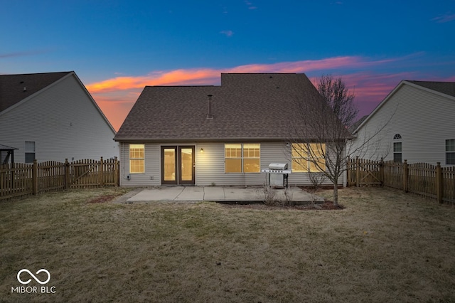 back of house at dusk with a patio area, a lawn, a fenced backyard, and roof with shingles