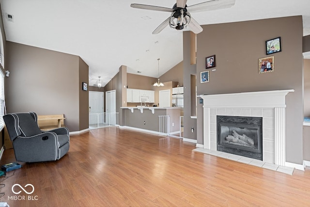 living area featuring ceiling fan, high vaulted ceiling, wood finished floors, baseboards, and a tiled fireplace