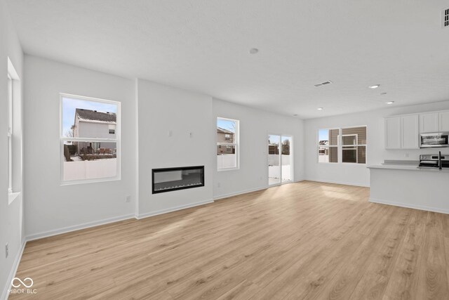 5119 Rolling Meadow Blvd, Indianapolis, IN 46237 - unfurnished living room with baseboards, visible vents, light wood-style flooring, and a glass covered fireplace