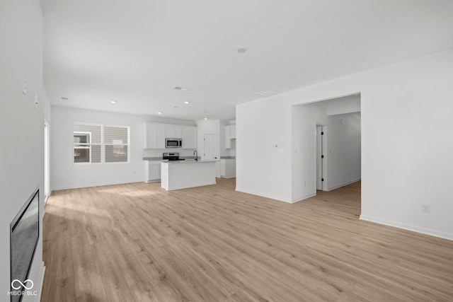 5119 Rolling Meadow Blvd, Indianapolis, IN 46237 - unfurnished living room featuring baseboards, recessed lighting, light wood-style flooring, and a sink
