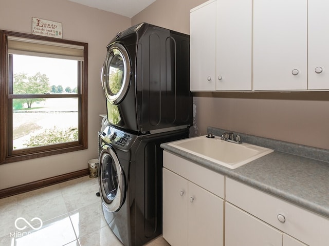 clothes washing area with light tile patterned floors, stacked washer / dryer, a sink, baseboards, and cabinet space