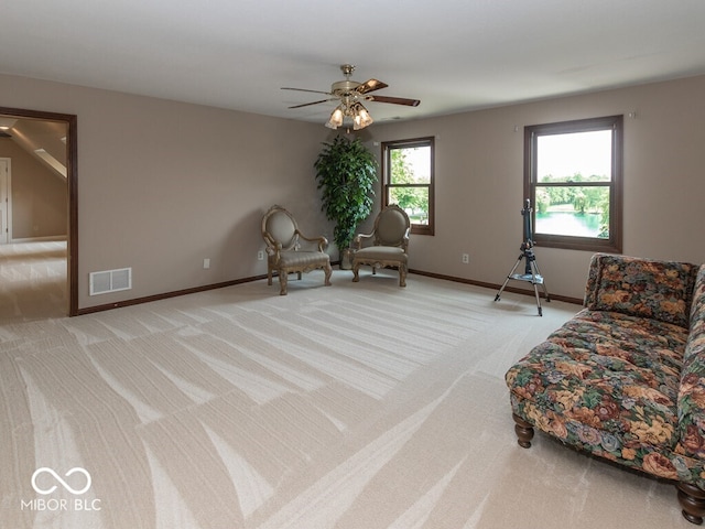 living area with light carpet, a ceiling fan, visible vents, and baseboards