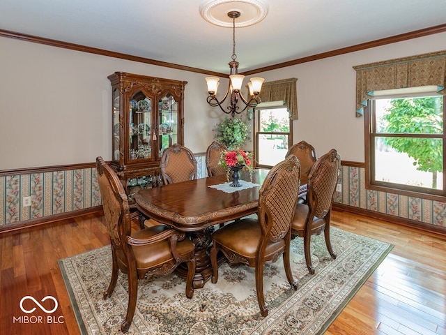 dining room featuring a wainscoted wall, light wood-style floors, wallpapered walls, an inviting chandelier, and crown molding