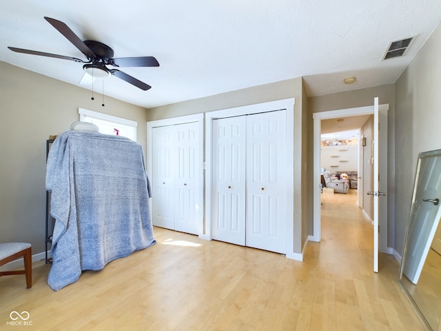 bedroom featuring multiple closets, visible vents, light wood-style floors, and baseboards