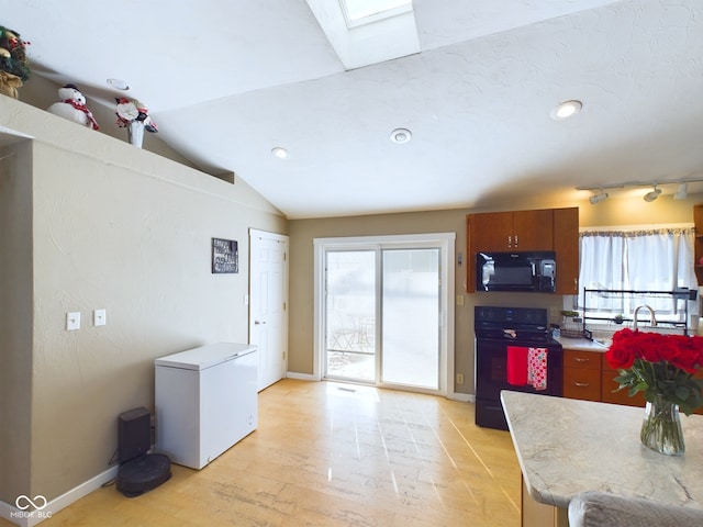 kitchen with a wealth of natural light, vaulted ceiling with skylight, light countertops, and black appliances