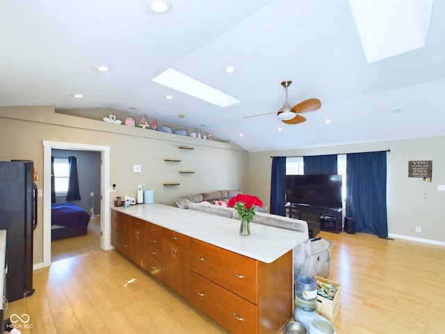 kitchen featuring lofted ceiling with skylight, open floor plan, freestanding refrigerator, a peninsula, and light countertops