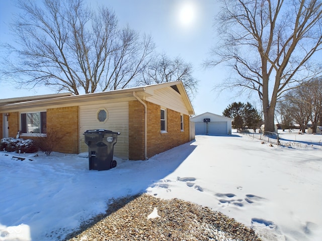 view of snow covered exterior with a garage, an outbuilding, and brick siding