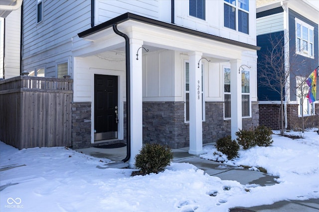 snow covered property entrance featuring stone siding