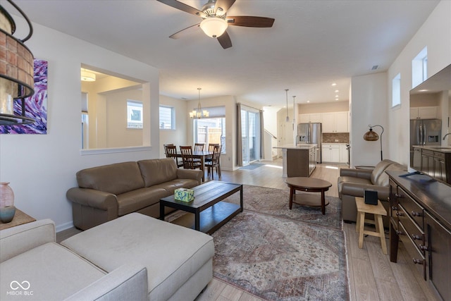 living area with ceiling fan with notable chandelier, recessed lighting, light wood-type flooring, and baseboards