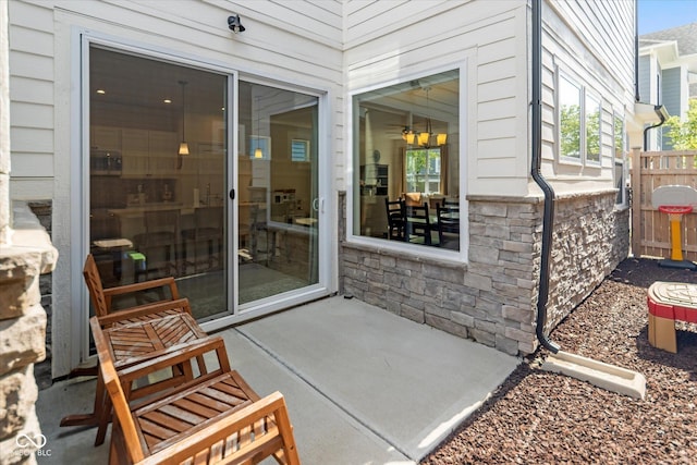 view of exterior entry featuring stone siding, a patio area, and fence