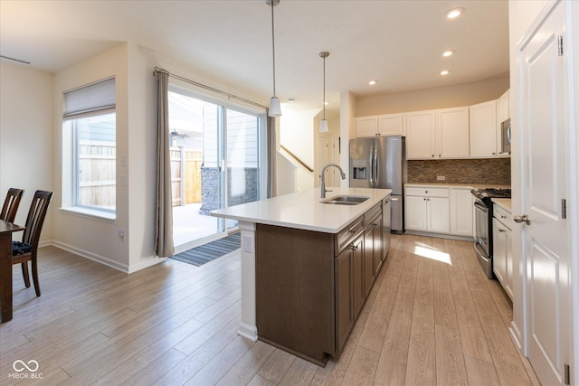 kitchen with white cabinets, appliances with stainless steel finishes, decorative light fixtures, light countertops, and a sink