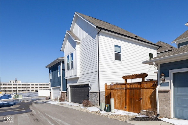 view of side of property with a garage, stone siding, a shingled roof, and board and batten siding