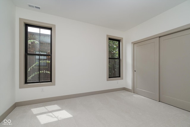 unfurnished bedroom with baseboards, visible vents, a closet, and light colored carpet