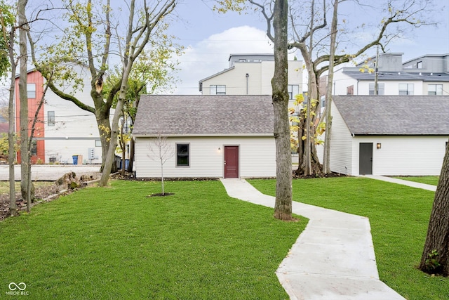 view of front of home with roof with shingles, an outdoor structure, and a front lawn