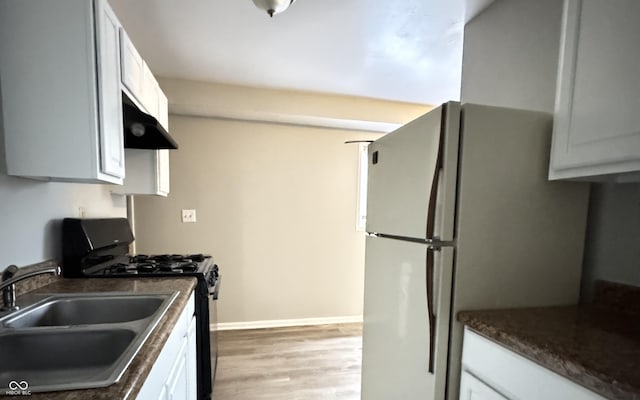 kitchen with dark countertops, range with gas stovetop, white cabinets, under cabinet range hood, and a sink