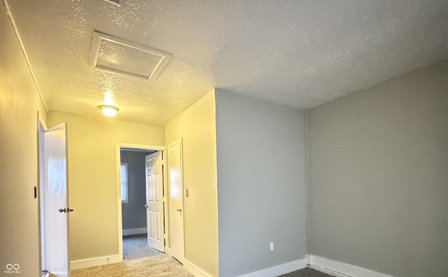 empty room with a textured ceiling, carpet floors, baseboards, and attic access