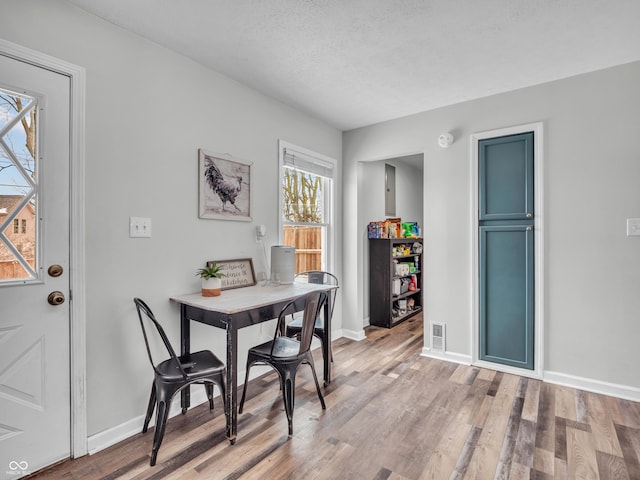 dining area with light wood-style flooring, visible vents, baseboards, and a textured ceiling