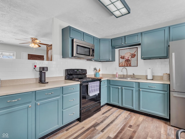 kitchen featuring a sink, light countertops, appliances with stainless steel finishes, blue cabinetry, and light wood-type flooring