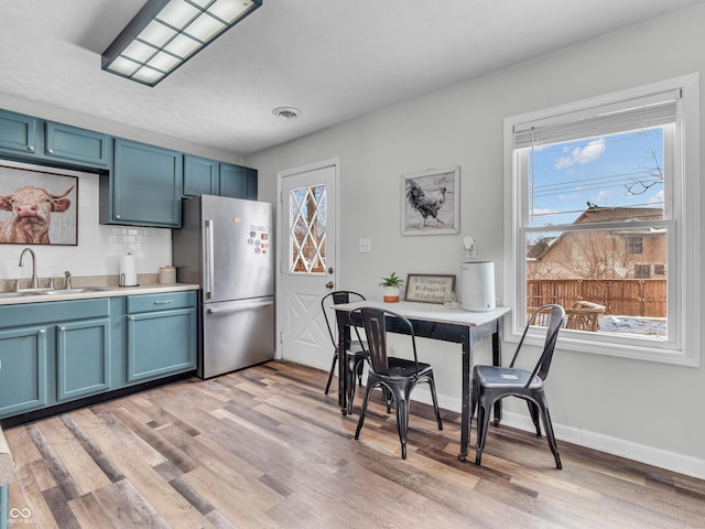 kitchen featuring light wood-style flooring, blue cabinets, a sink, light countertops, and freestanding refrigerator