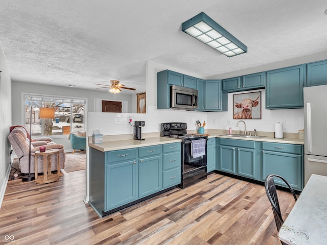 kitchen featuring light wood finished floors, stainless steel appliances, light countertops, a sink, and blue cabinets