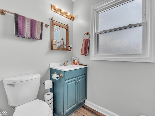 half bath featuring toilet, vanity, baseboards, and wood finished floors