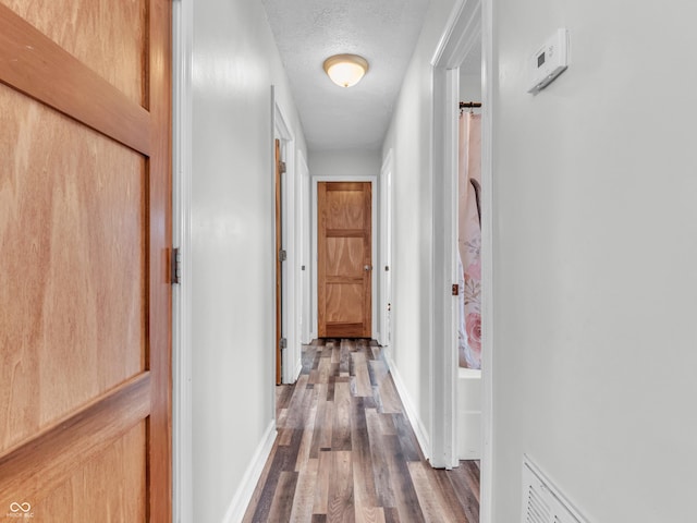 hall featuring a textured ceiling, dark wood finished floors, visible vents, and baseboards