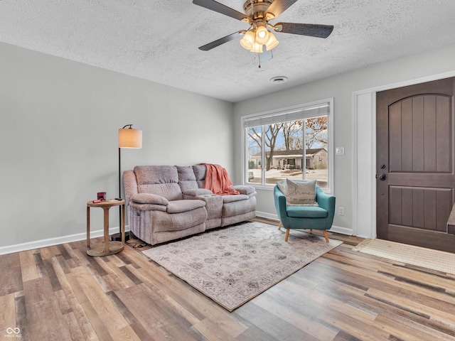 living room with a textured ceiling, baseboards, and wood finished floors