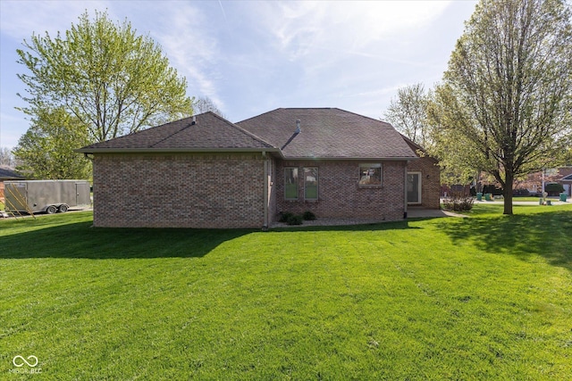 back of house featuring a lawn, a shingled roof, and brick siding